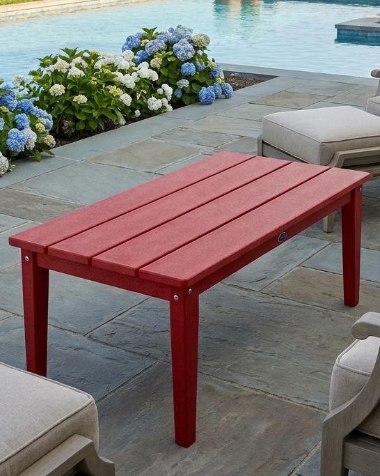 Red outdoor table on a stone patio with flowers and chairs in the background.