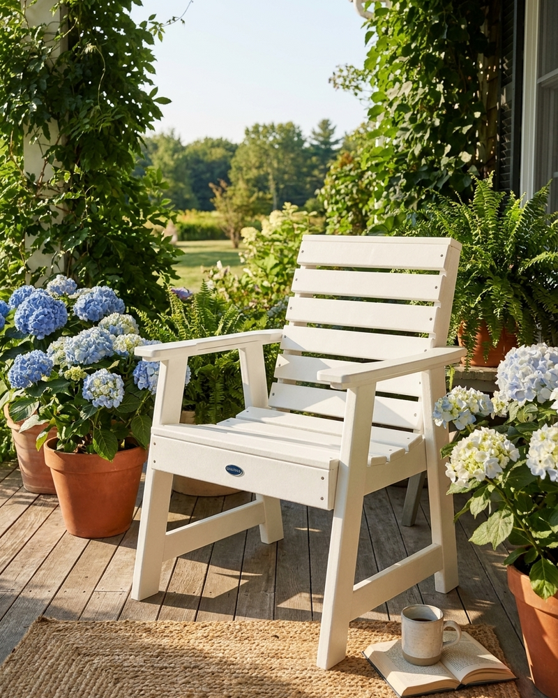 White chair on a wooden deck with potted flowers and a cup of coffee.