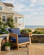 Toscana teak swivel chair with navy cushion on stone patio near a  coastal home with views of the ocean.  